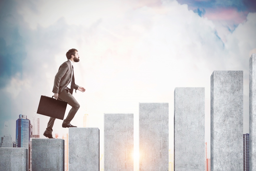Side view of a businessman climbing concrete columns built like steps.