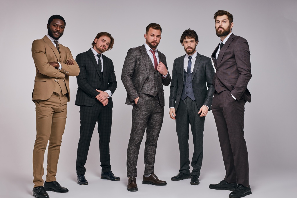 Five young businessmen in suits pose together in a studio setting.